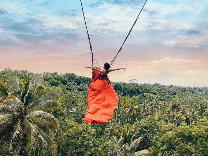 Ca sĩ 9X diện một chiếc đầm maxi đỏ, "tung bay" trên Bali Swing được mệnh danh là "xích đu tử thần", hấp dẫn người ưa chơi trò mạo hiểm. Khung cảnh núi rừng bao quanh, phía trên là bầu trời, dễ dàng giúp bạn tậu được bức ảnh "chất lừ". Đây là một trong những điểm đến hút du khách nhất Bali mà mùa cao điểm, đôi khi bạn phải xếp hàng rất lâu mới đến lượt trải nghiệm.